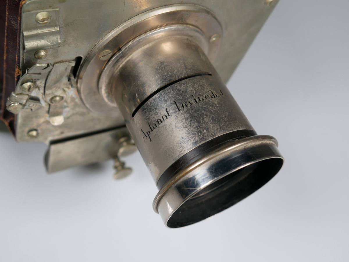 Bälgkamera med tillbehör. 
Kameran är märkt H. MADER'S Patent INVINCIBEL Model II
Modellen är den första vikbara kameramodellen och tillverkades 1888-1890. 
Väska och tillbehör är original. 

Objektivet är märkt Aplanat Invincibel. Har skåra där bländare (AM 2022-033-C) kan placeras. Bländaren har 6 valbara bländaröppningar. 

Väskan är av canvas med läderdetaljer och har ett trasigt axelband. 
AM 2022-033-A: Kamera
AM 2022-033-B: Objektiv
AM 2022-033-C: Bländare
AM 2022-033-D: Hårkors
AM 2022-033-E: Stativ
AM 2022-033-F: Väska
AM 2022-033-G:1-6: Kassetter till glasplåtar