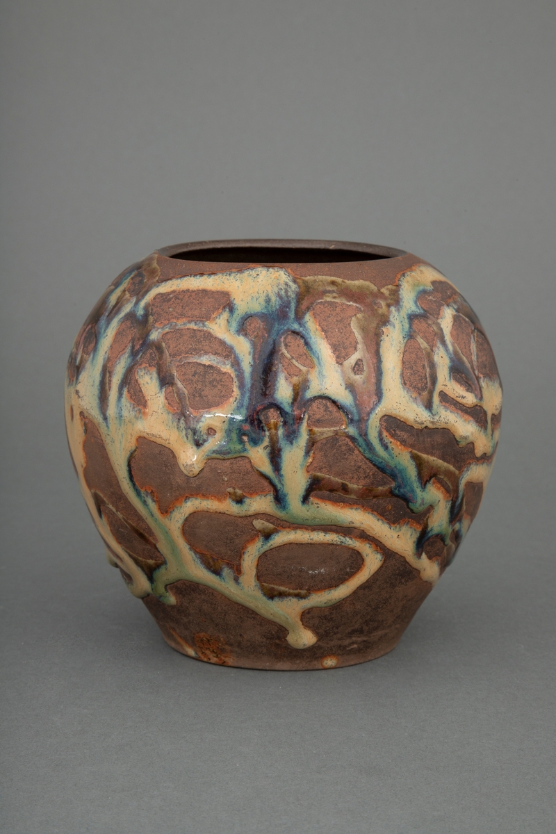 Kuleformet vase til bruk for blomster. smal åpning. Gråbrunt, hardt og tett gods. Utvendige årer av fritt flytende glasur, gulbrun, iblandet brunt og mørkeblått med metallisk skimmer.