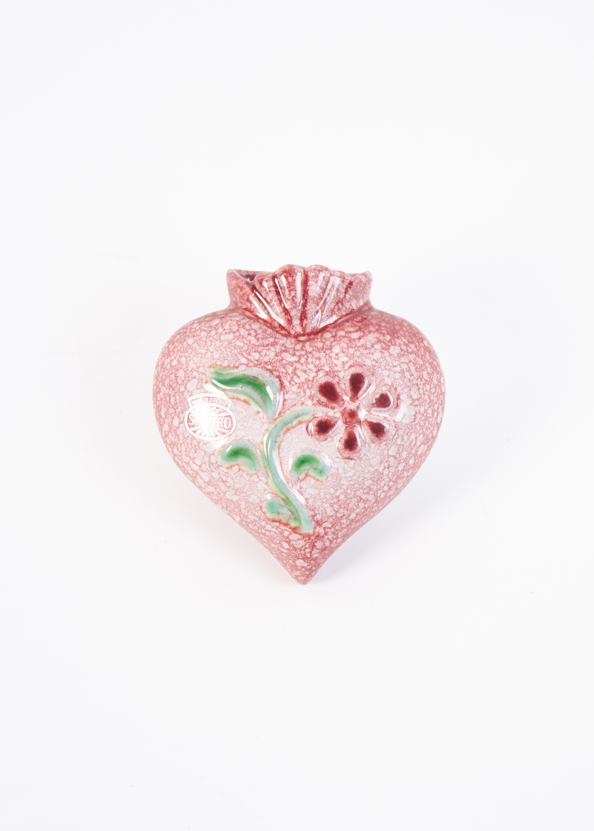 Hjerteformet, rosa-/rødspettet veggvase med rød blomst med grønne blader.