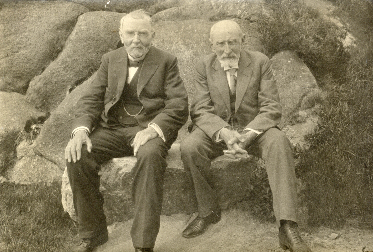Portrett av to eldre herrer sittende på en stenbenk.