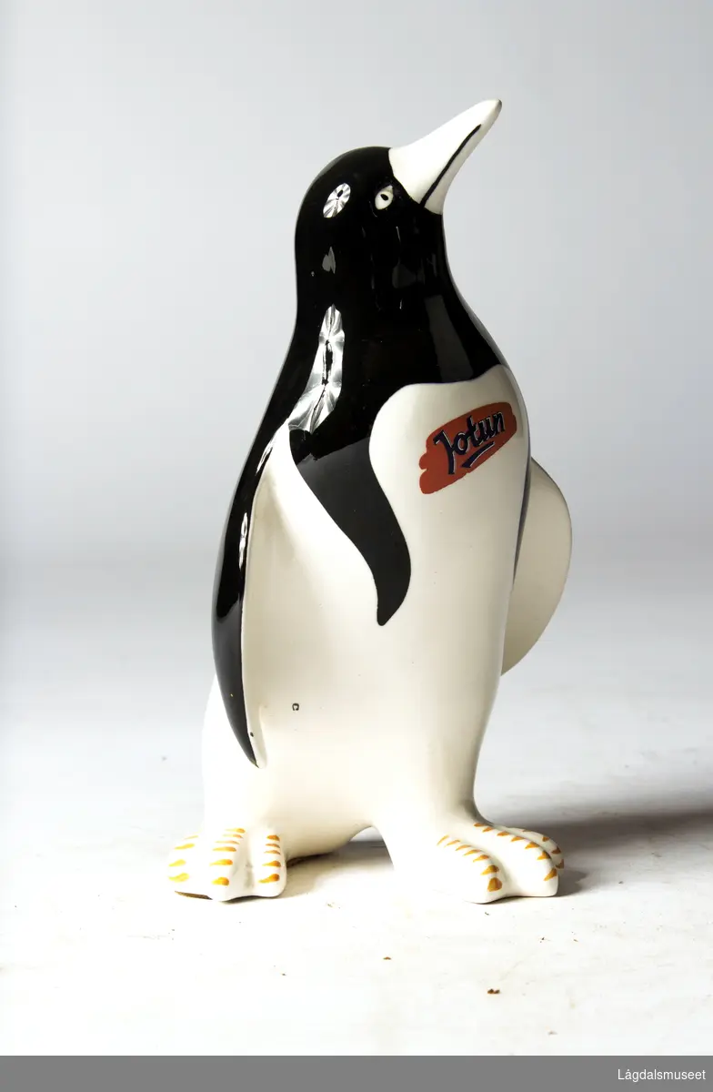 Pingvin i fajanse med firmalogo for Jotun i blå bokstaver på oransje bakgrunn på brystet til pingvinen.