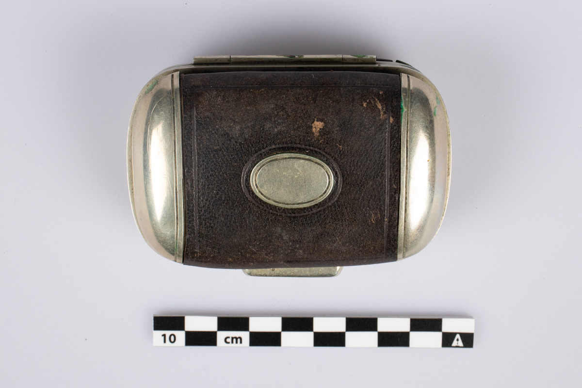 Liten lommebok i metall med låsemekanisme og preget brunt skinn på utsiden 