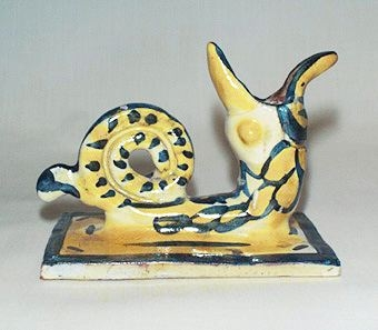 Ljusstake, föreställande ett odjur, av lergods i gul och blå färgsättning.