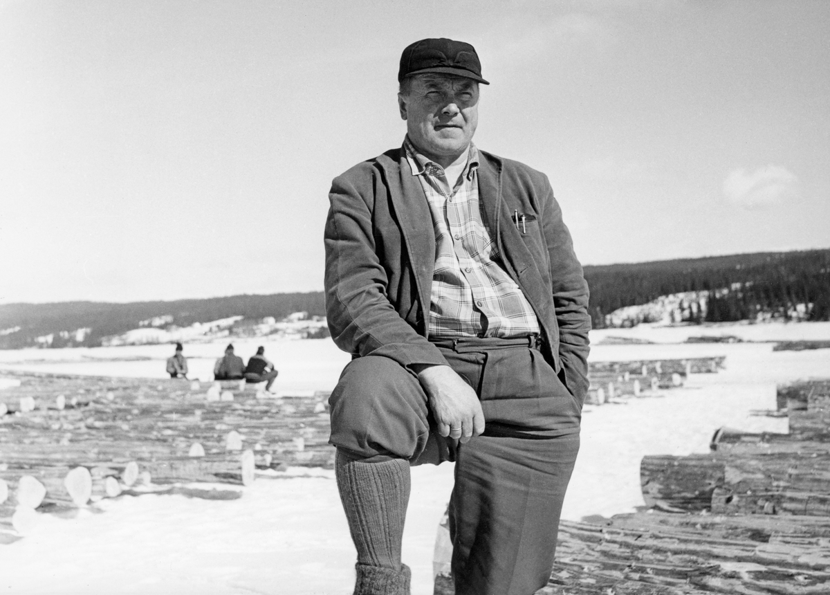 Bildet viser distriktssjef for distrikt 2 i Glommens Tømmermåling, Petter Borg (1908-1979), på tømmervelta ved Osensjøen i april 1961. I forgrunnen ses barket tømmer lagt opp på isen klargjort for merking og fløting på sjøen seinere på våren.