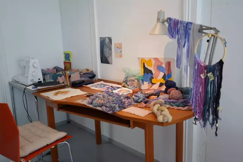 Bildet viser er arbeidsbord med symaskin, garnspoler, pensler og kunstverk.
