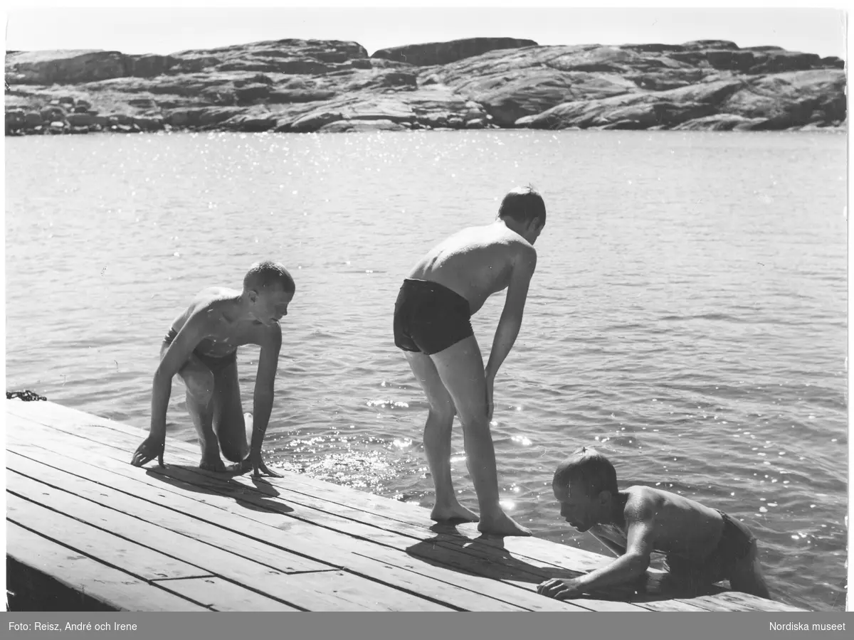 Tre pojkar badar vid en brygga i Fisketången.