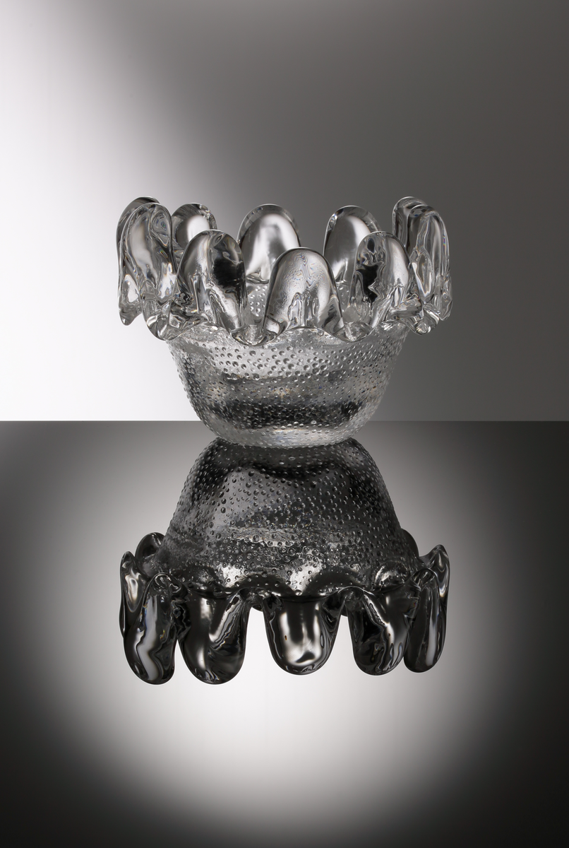 "Solros", formgiven av Göran och Ann Wärff. Ofärgat glas. SKålen är delvis gjord i en hyttarbetad teknik som innebär att ovandelen, på den stiliserade blomman, har runnit ut av egen kraft. Därför blir alla glas i Solros-serien unika i sitt uttryck.