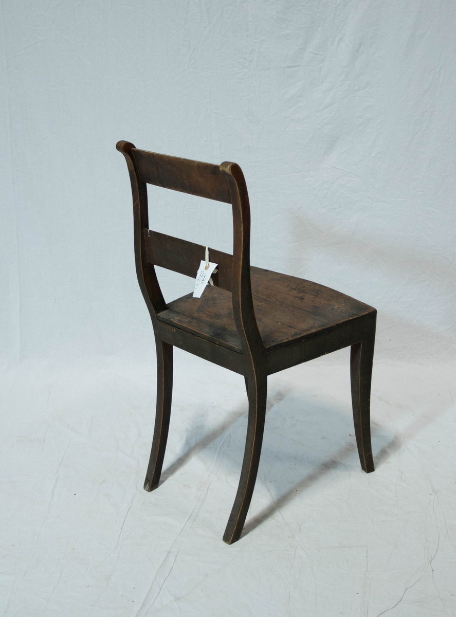 Stol av tre. Stolen har fire sabelformede og krummede ben, glatte sidesprosses. Ryggstavene til stolen er  S-svungne og forbundet med to glatte og horisontale bretter. Setets fremkant er horisontalt buet.