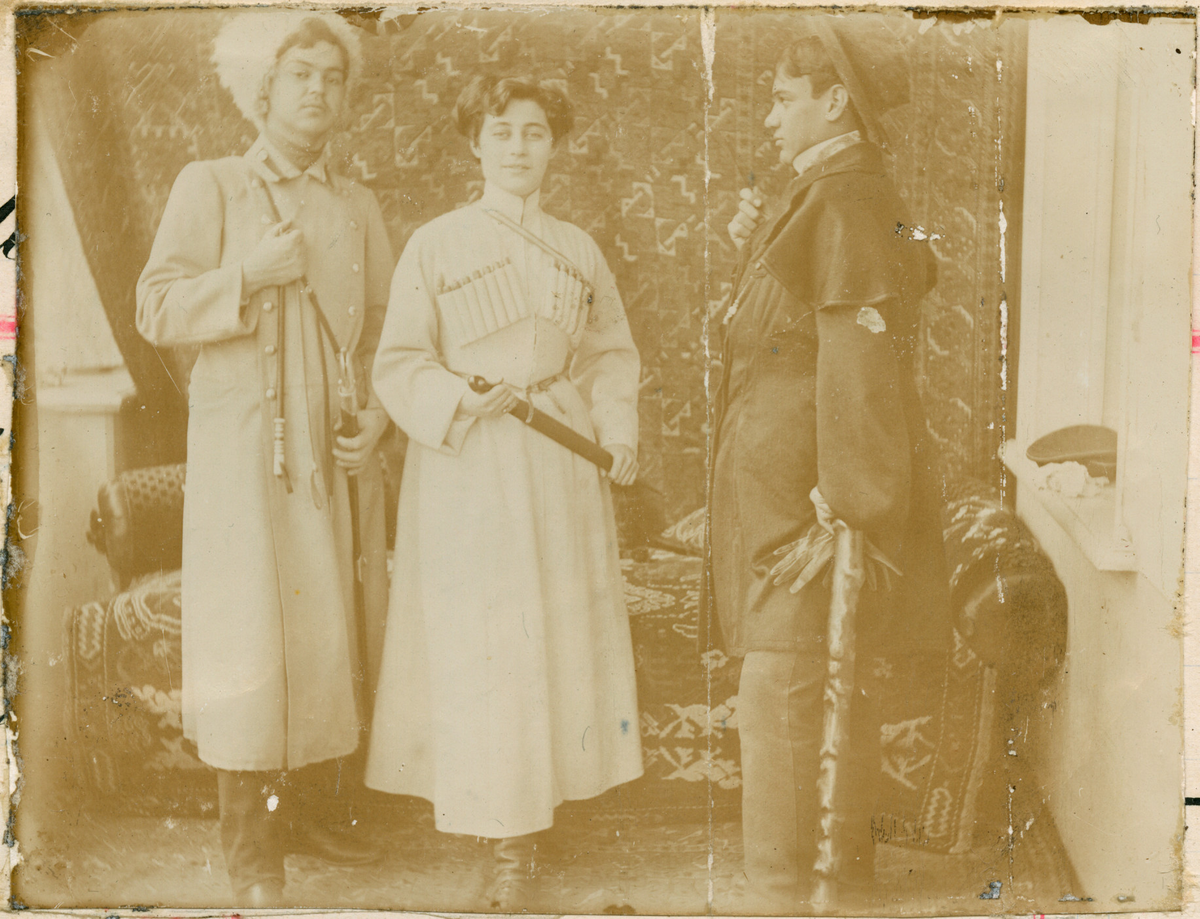 Florentine Rostin og to ukjente unge menn poserer foran et veggteppe og en sofa i uniformlignende klær. I vinduskarmen til høyre ligger en uniformlue. Mannen til høyre i bildet holder et par hansker. Mannen til venstre er ikledd en russisk kosakk-lue.