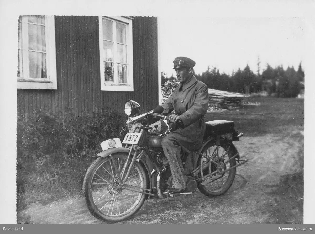 En man med skärmmössa sitter på en motorcykel med registreringsnummer Y572, på gårdsplanen invid en husknut. Ur en samling som tillhört Astrid Hermansson/Selin, Svartvik.