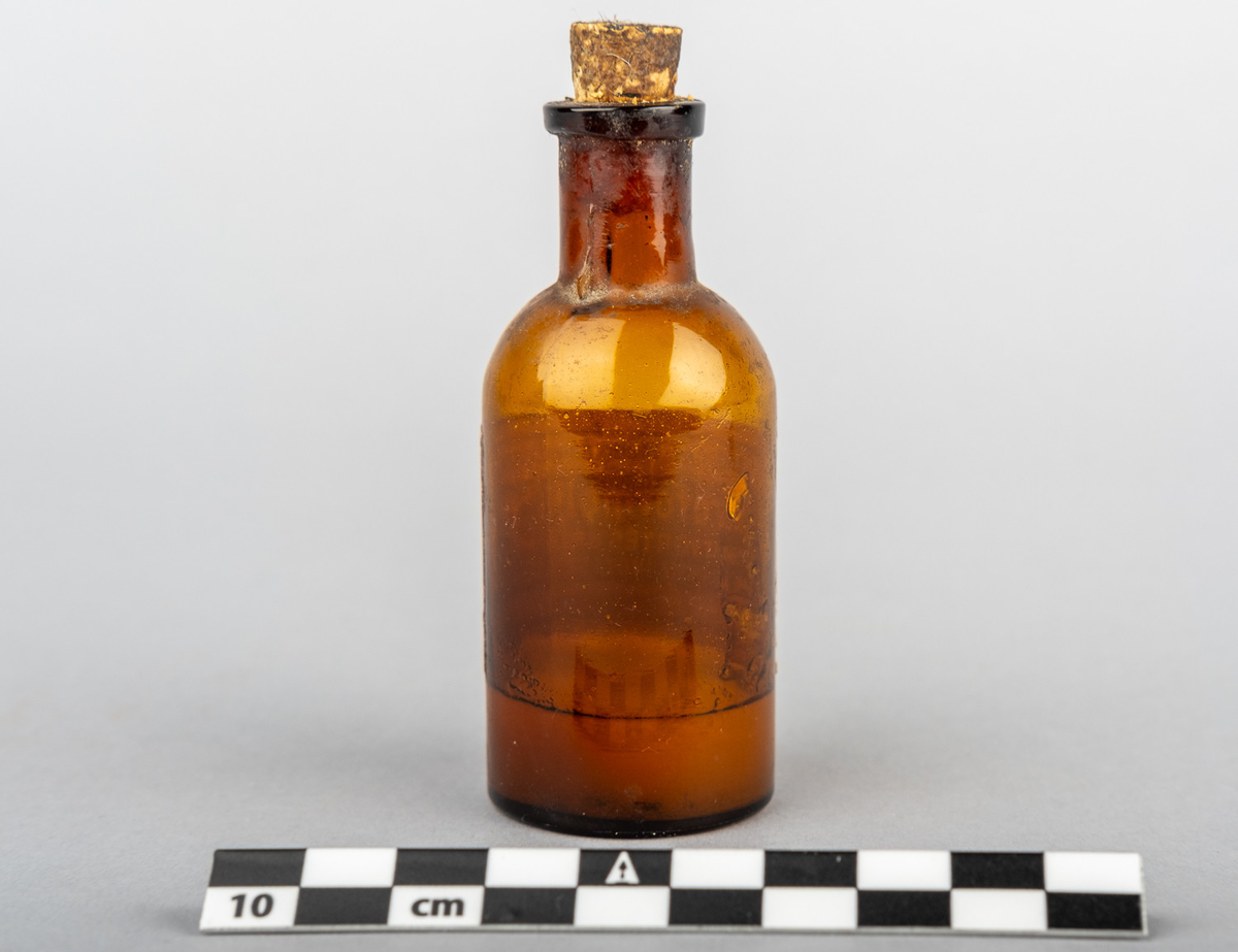 Medisinflaske, brun med kork og innhold. Merkelapp som identifiserer innhold som kloroform. 