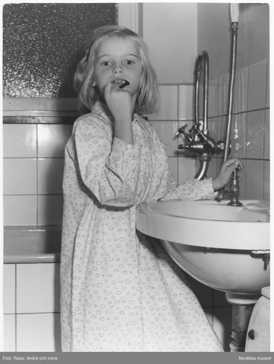 En flicka i nattlinne står vid tvättfatet i badrummet och borstar tänderna.