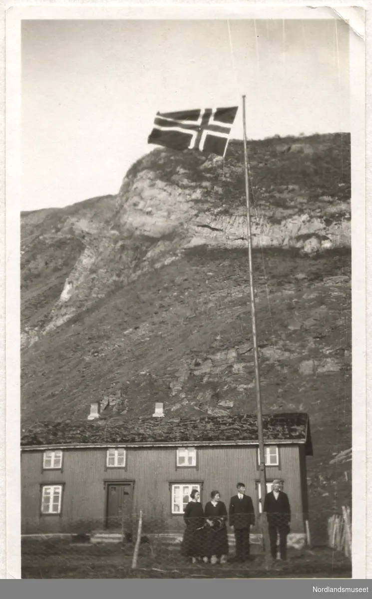To menn og to kvinner står foran et nordlandshus, flagget er heist høyt til værs