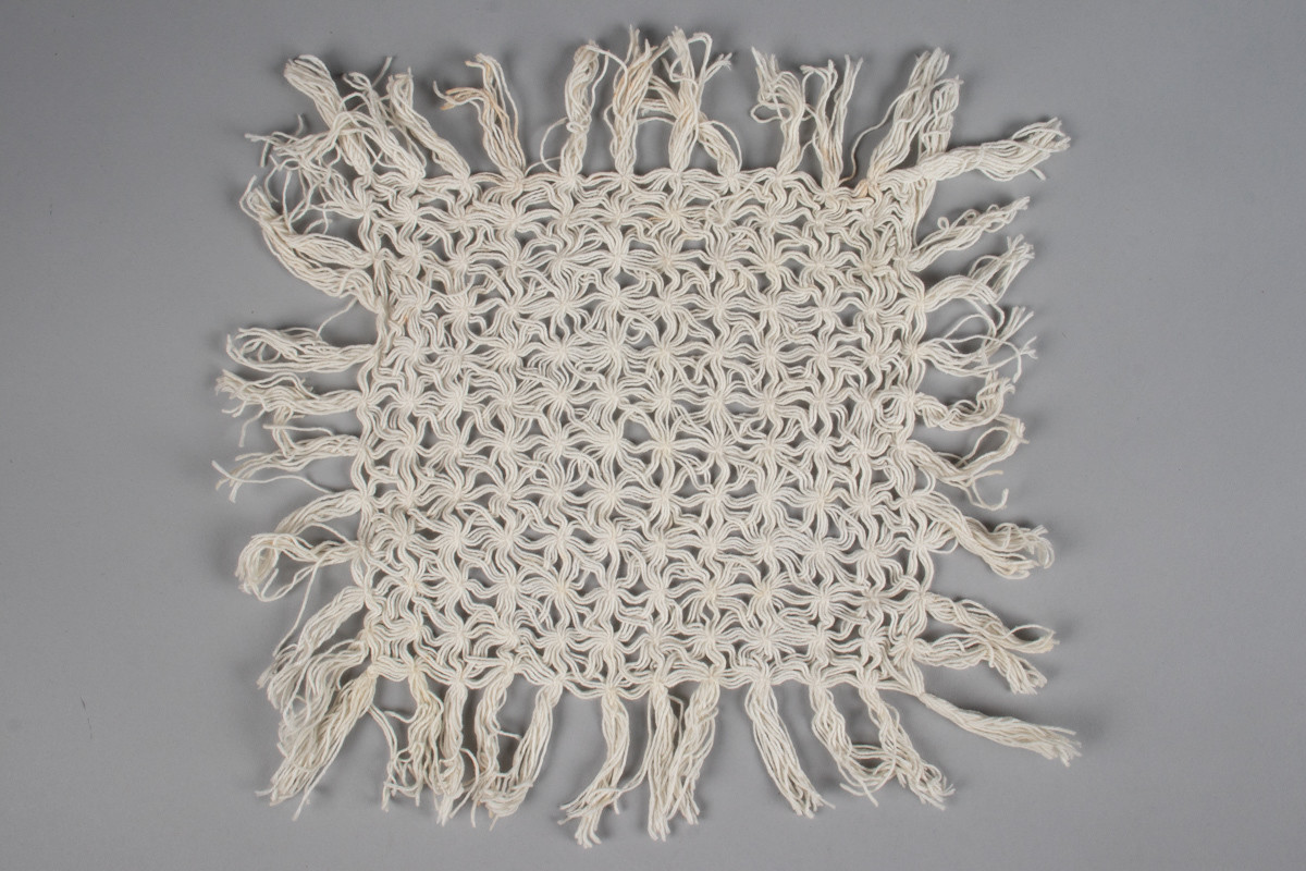 Rektangulær duk med knutemønster og frynser. Laget av bomullstråd. Knytteteknikk