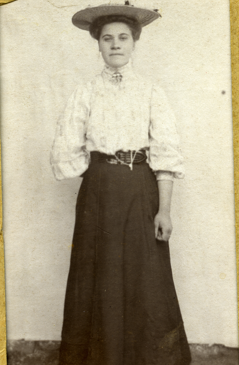 Portrett av Kristi Hallibakken med hatt, bluse og skjørt.
