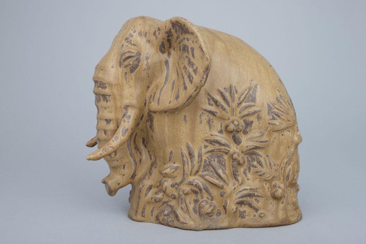 Keramikkfigur i finkornet tett gods med grålig farge. Glasert i gulbrun med mørkere sjatteringer. Skulpturen forestiller en elefant.