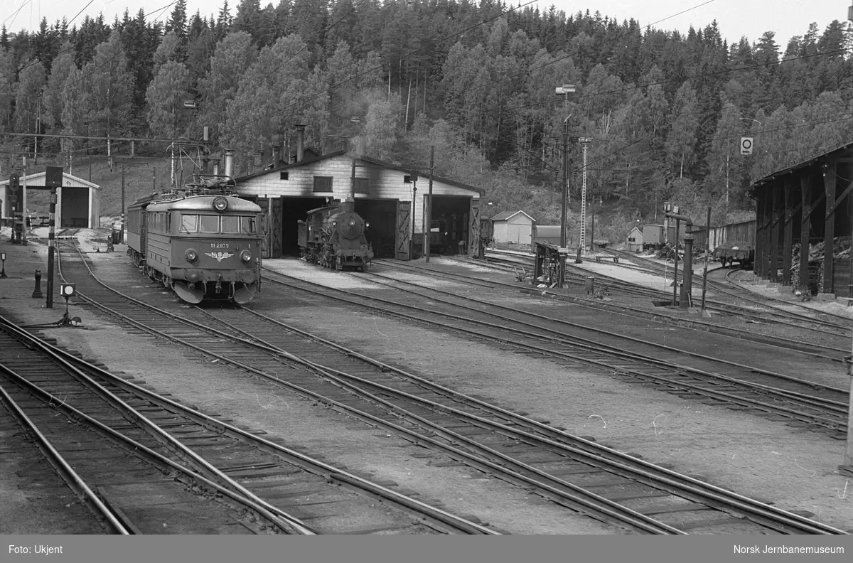 Elektrisk lokomotiv El 11 2109 foran lokomotivstallen på Hønefoss stasjon. Til høyre damplokomotiv type 24