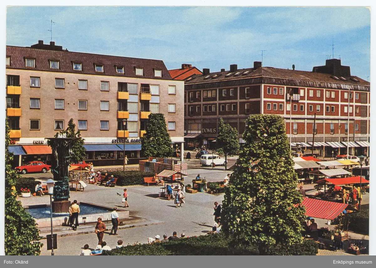 Vykort i färg med motiv av Stora torget, Enköping. I bild ser vi lite av Torggatan och Kungsgatan. Årtal osäkert, men förlaget som tillverkade vykortet fanns mellan åren 1961- 1981. Så någon gång däremellan är bilden fotograferad.