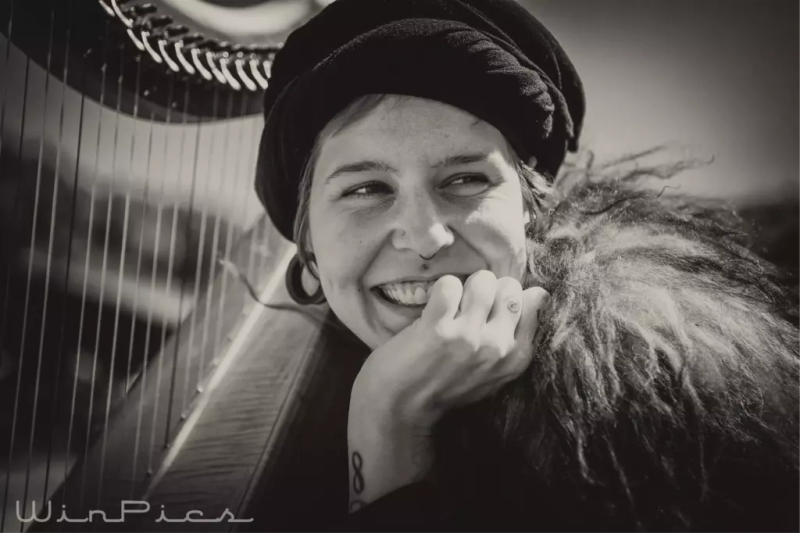 Svart-hvitt portrett av ung kvinne som sitter med en harpe inntil seg og hviler haken i venstre hånd.