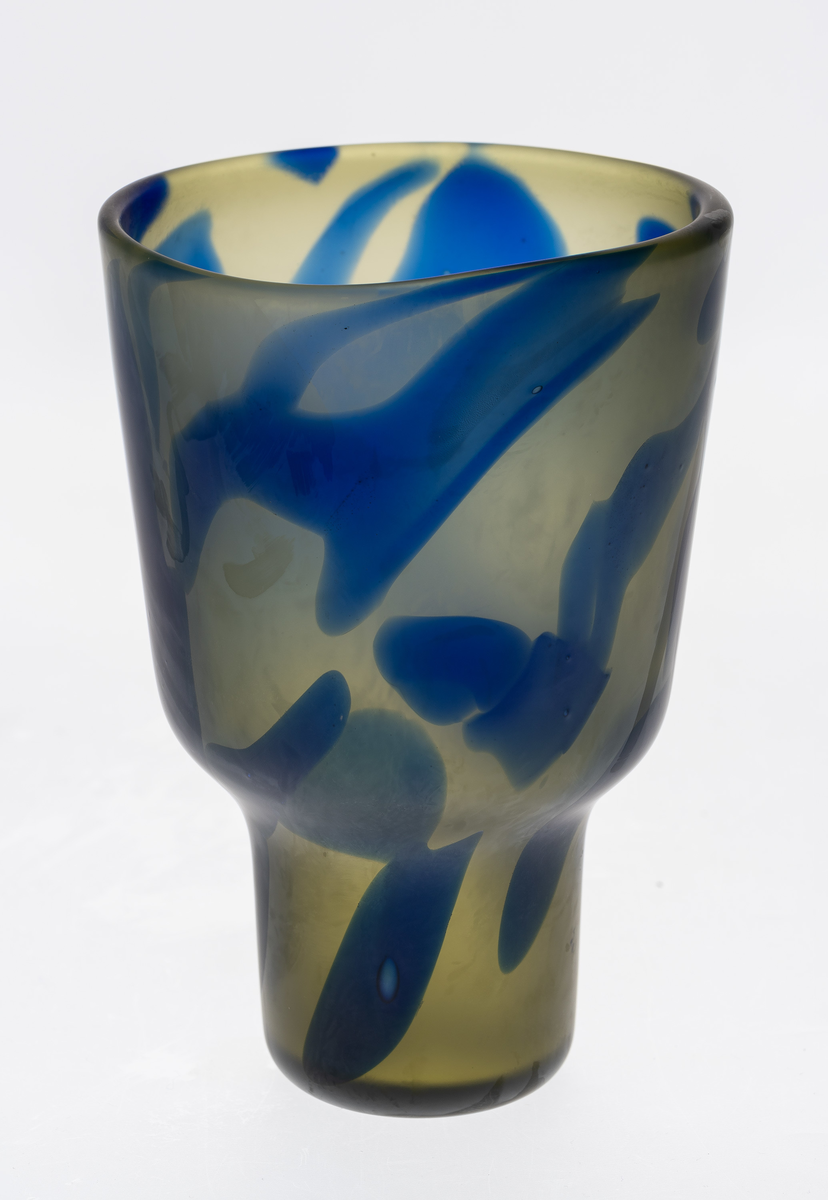 Vase i halvgjennomskinnelig farget glass med overfang. Korpus består av to koniske deler, utført i gulgrønt glass med blåfargede partier, hvis ytterside er mattet med syre.