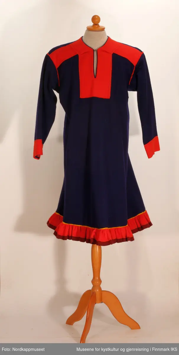 En samisk kvinnekofte (nissungàkti) sydd av blått ullstoff, med en holbi-koftekant av rødt, mørkerødt og gult. 

På ryggen, skuldrene, kragen og rundt halsåpningen er det sydd brede border av rødt ullstoff. 

Koften er sydd i Jergul, Karasjok.