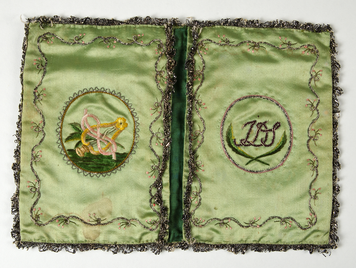 Plånbok av grönt siden med silkebroderier i stjälksöm och kedjesöm i flera färger. På framsidan och baksidan blommotiv, på insidan medaljongen, den ena med monogram I D S. Fodart med mörkare grönt siden. Kantad med silverspets.