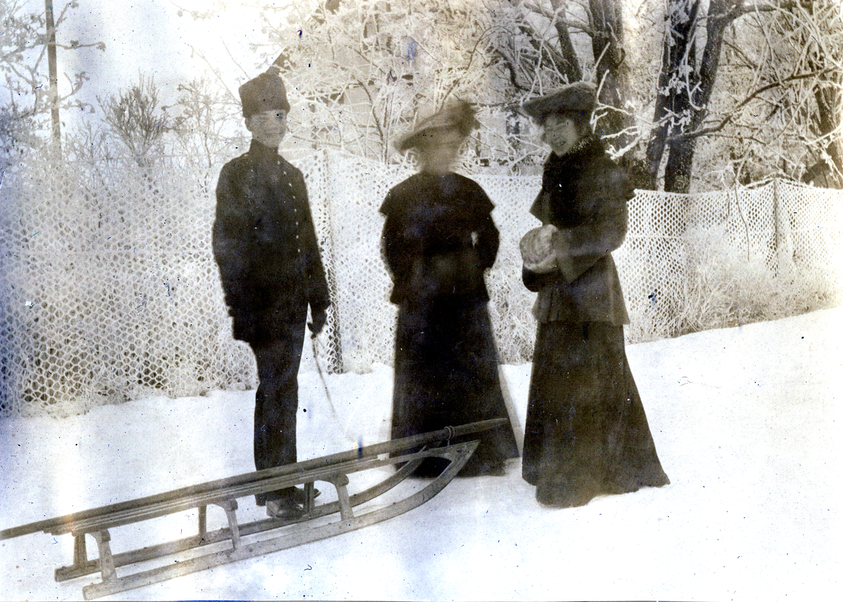 En ung mann med lang kjelke, Aagot Henriksen (f. 1880(?)) og Sigrid Svendsen (Sæthern?) står ute, vinter 1903.
Bilde er fra fotoalbum GM.036887.