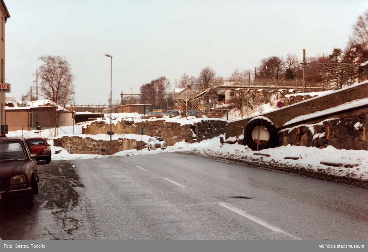 Mölndals Kvarnby i januari 1984. Parkerade bilar på Pixbovägen utanför byggnaden "Strumpan". Till höger gångbro över järnvägen.