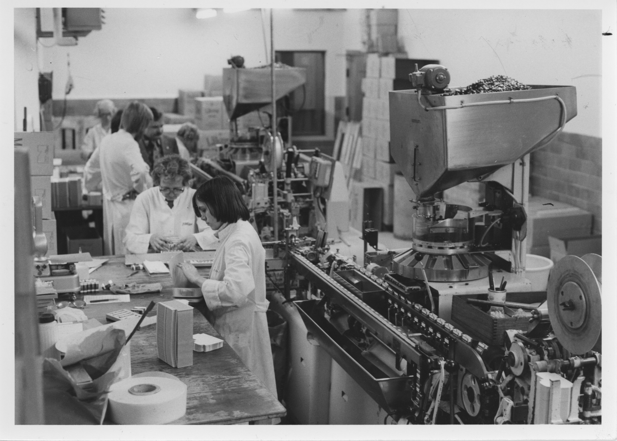 Askpackningen i Danmark november 1977. Arencomaskin packar Läkeroltabletter. Flera kvinnor handpackar och sköter maskinen.