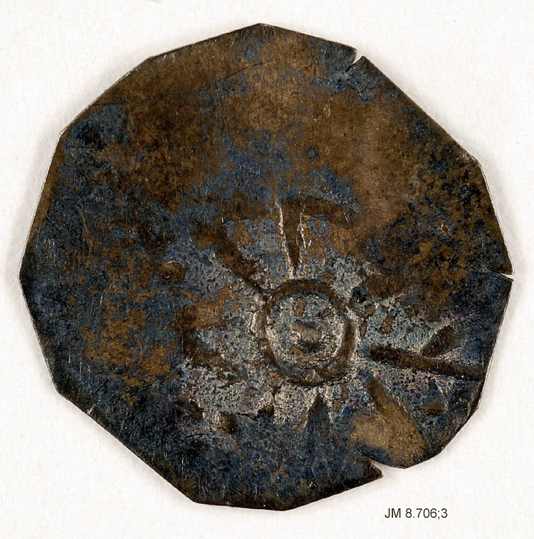 Silvermynt, till synes endast präglat på ena sidan med ett runt kors med prick i mitten och dubbellinjigt kors, ingen omskrift. Eventuellt är detta mynt från 1220-30-talen (Ulf Jarl) då man slog både dubbelsidiga som ensida mynt. Dessa beskrivs som en ring med en punkt i mitten, och med dubbellinjigt kors.