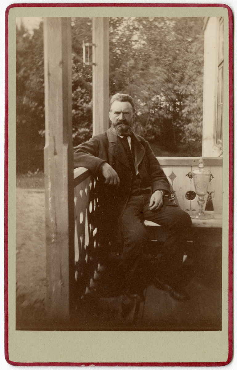 Foto av byggmester Nestor Malthe sittende mot gelender på Dal gård, trolig slutten av 1870-tallet