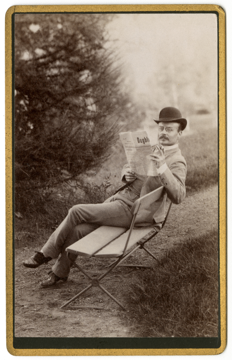 Foto av Jørgen Dahl som sitter på benk og leser avis med en sigar i hånden, antagelig på Dal gård