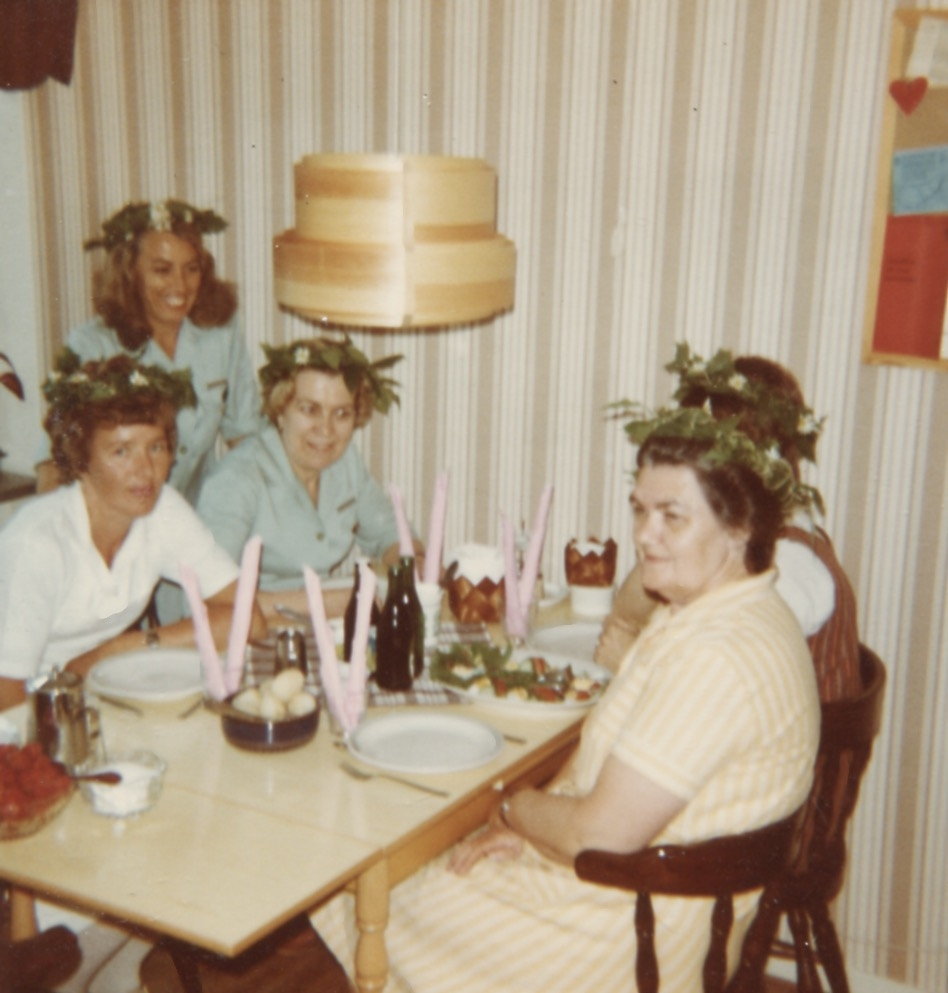 Brattåshemmets personal sitter och äter vid ett bord 1970 - 1980-tal. 1. Föreståndare Rose-Marie. 2. Okänd kvinna (stående). 3. Hildur Berntsson. 4. Skymd kvinna. 5. Ögren?