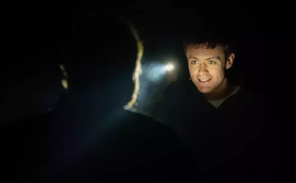 Nærbilde av ansiktet til en mann som lyser opp når han finner en annen mann i lyset fra lommelykta.