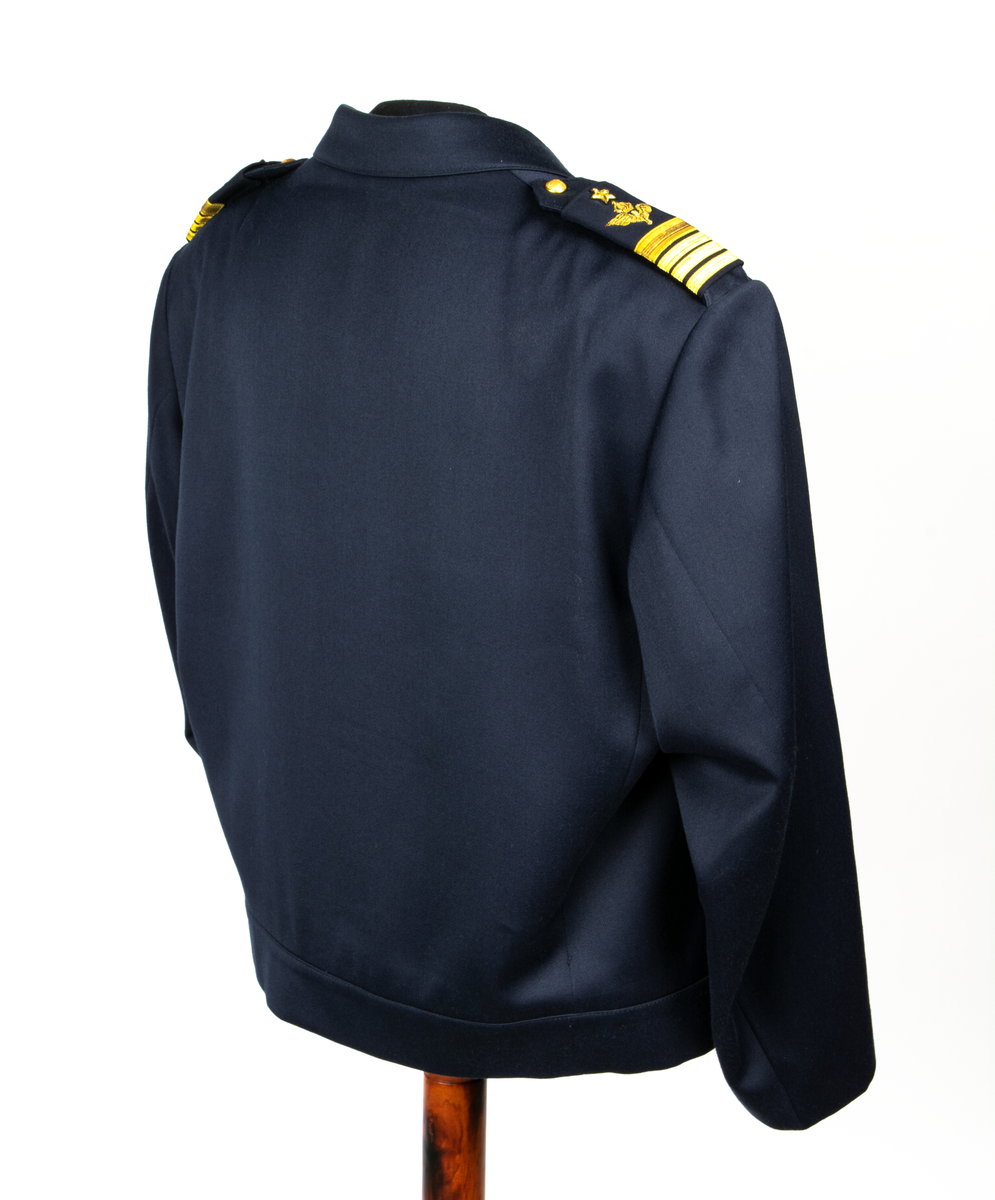 Jacka m/87. Blå uniformsjacka med dold knäppning med fyra knappar av plast. Jackan har midjelinning, fasta axelklaffar vilka försetts med försetts med gradbeteckning, överste 1 graden.  På vänster överarm är en nationsbeteckning i form av en svensk flagga fastsydd och på höger bröstficka sitter försvarsstabsmärke m/49.