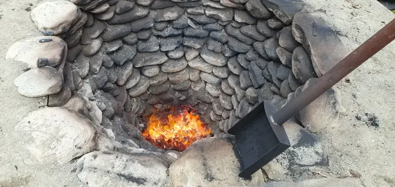 Bildet viser et ildsted murt opp med stein. Det er et redskap på siden av bildet.