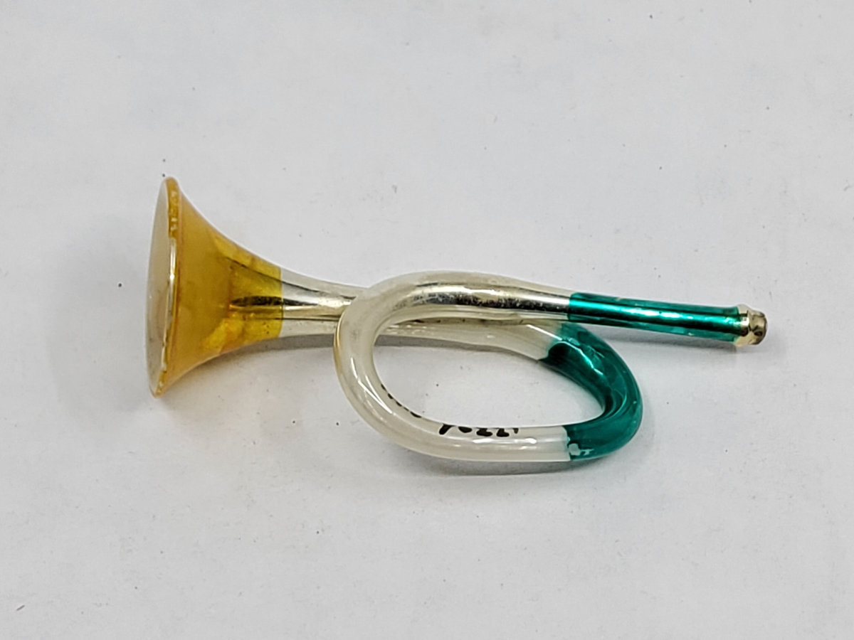 Julgransprydnad. Trumpet av celloluid, silver-, -gul och grönfärgad.