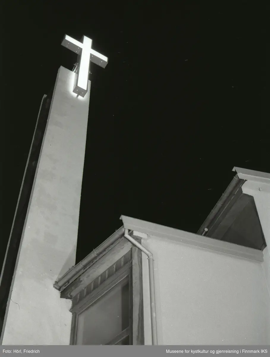 Det lyssatte korset til den nybygde katolske kirken St. Mikael i Hammerfest skinner i natten. Bildet er tatt fra gateplan i Strandgata og oppover.