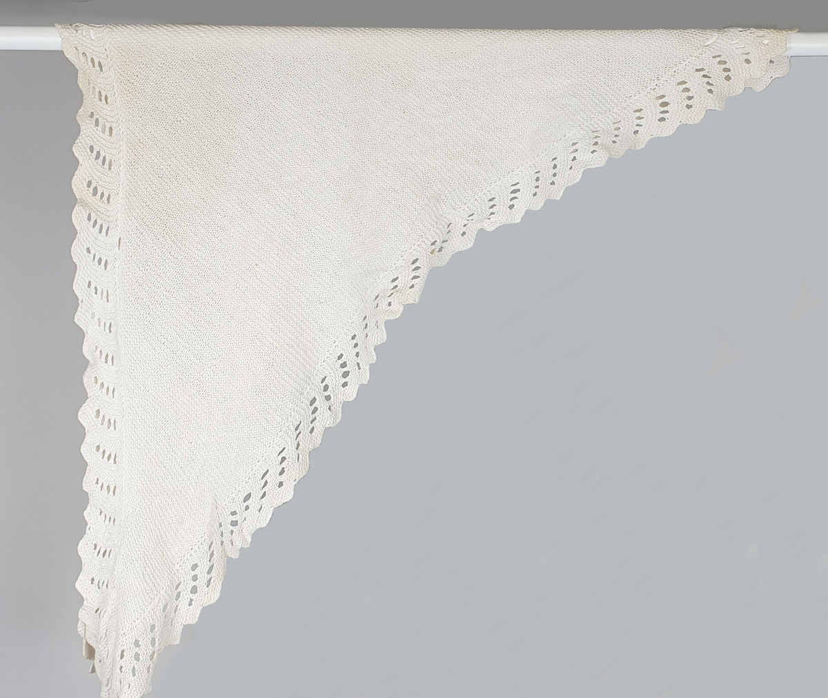 Hvitt, trekantet sjal (tørkle) av bomull, håndstrikket med hullbord langs ytterkantene.