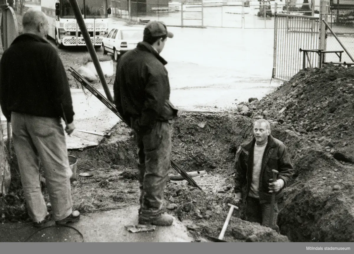 Under tiden nya Teaterhuset byggdes 1997 – 1998. Bilden är utomhus där en person grävt en stor grop som han står i. I handen håller han en spade. Bakom gropen som mannen står i är det en stor jordhög. Janne Sandberg, amatörteaterkonsulent, samt en okänd man står till vänster om gropen.