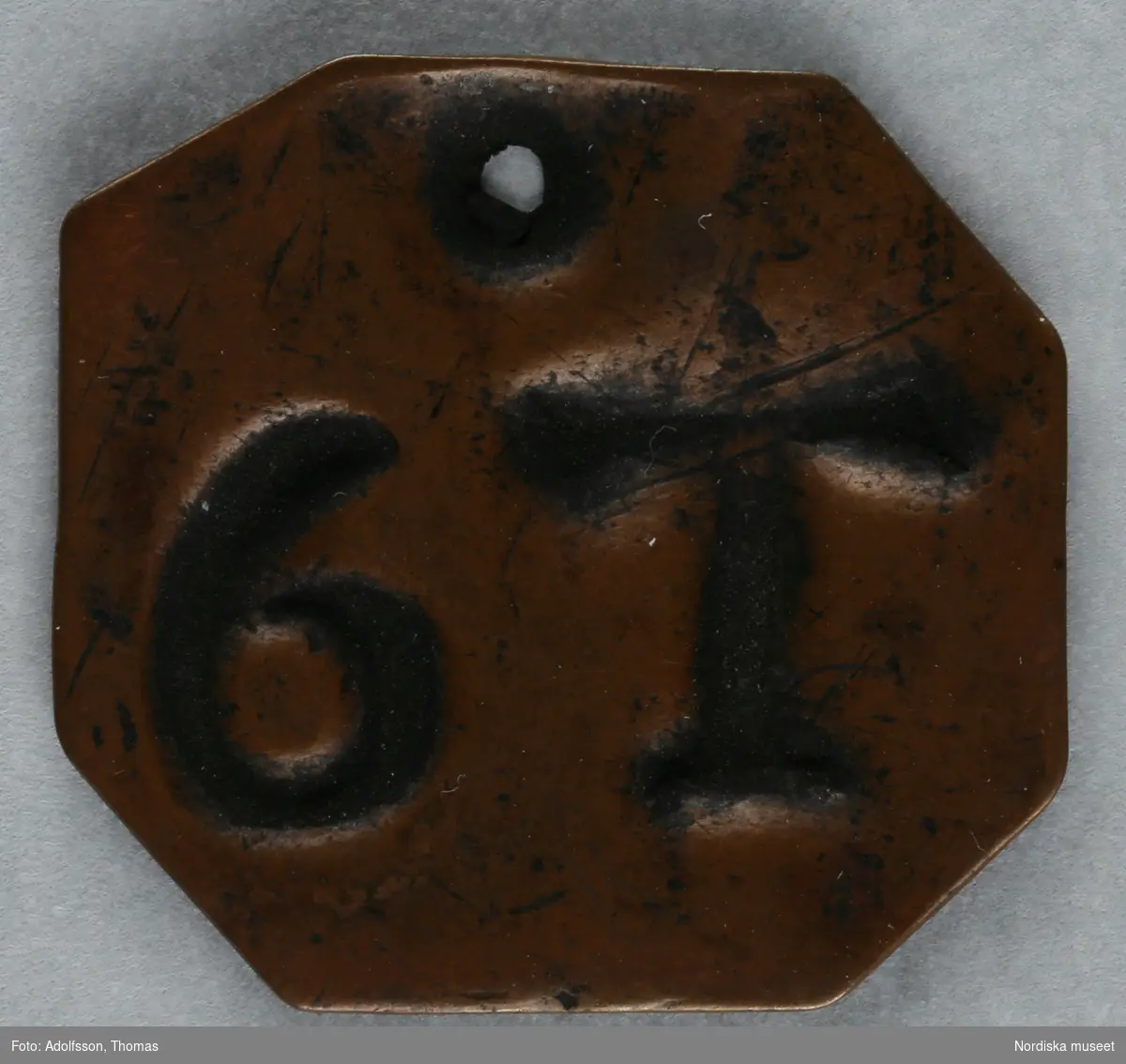 Pollett, av koppar, fyrkantig med avklippta hörn, ett hål, präglad text: "6 T".