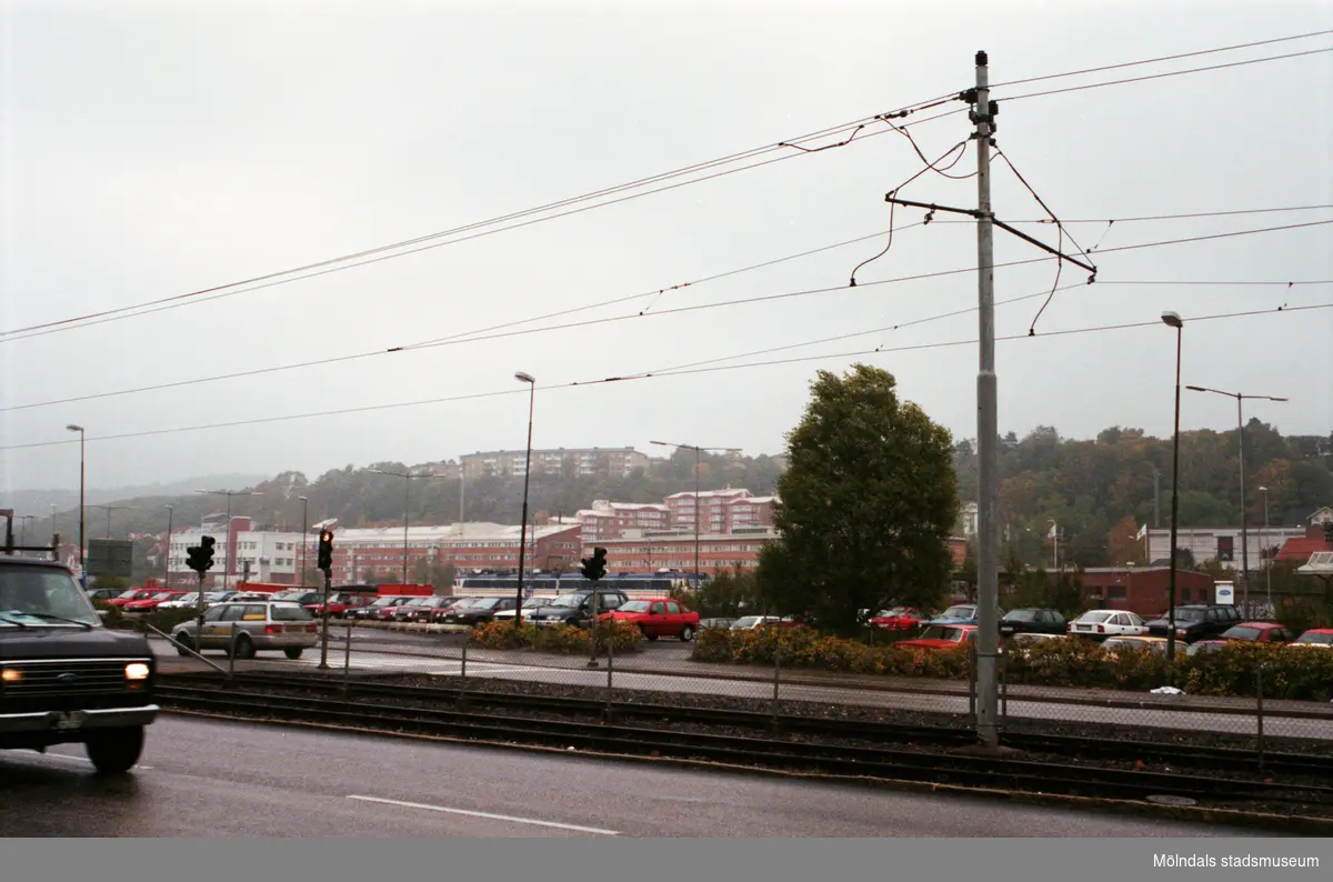 Bilar kör på Göteborgsvägen. I bakgrunden ses Södra Ågatans parkering. Mölndalsbro i dag - ett skolpedagogiskt dokumentationsprojekt på Mölndals museum under oktober 1996. 1996_1173-1187 är gjorda av högstadieelever från Kvarnbyskolan 9D, grupp 3. Se även 1996_0913-0940.