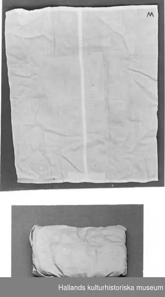 Föremålsposten avser magasinsplacering för del C) täcke.

Sängkläder. a) Kudde av ljusblått tyg. Längd: 12 cm, bredd: 10 cm, tjocklek: 1,5 cm. b) Örngott med spets av vitt bomull med rött monogram: "T. S." Längd: 15 cm, bredd: 13 cm. c) Täcke, stickat, blått. Längd: 37 cm, bredd: 20 cm. d) Överlakan, vitt bomull med spets. Längd: 49 cm, bredd: 30 cm. e) Underlakan av vitt bomull märkt med rött i ena hörnet med: "M".Längd: 38 cm, bredd: 31 cm. f) Madrass av ljusblått tyg. Längd: 20 cm, bredd: 13 cm, tjocklek: 2 cm.