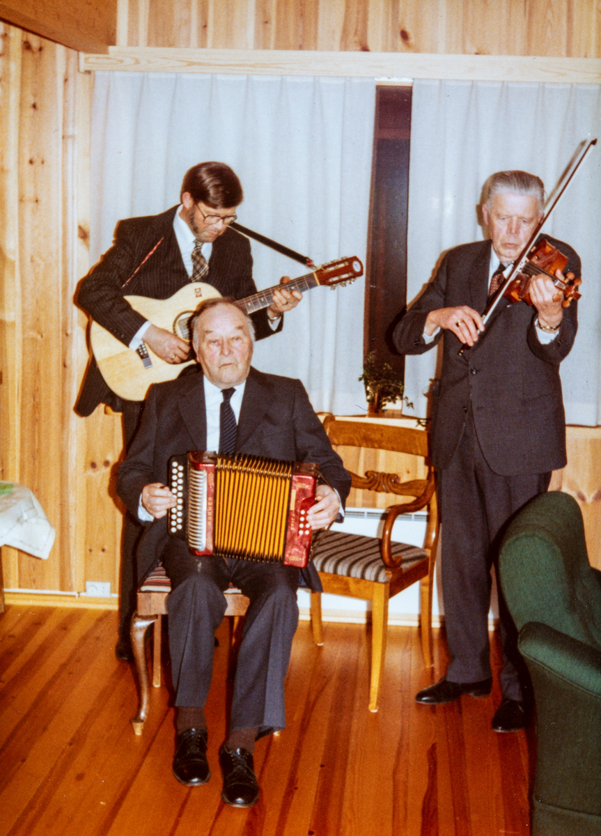En lokal musikk trio underholder på medlemsmøte i Ottestad pensjonistforening rundt 1980.
Fra venstre: på gitar: Kjell Mangerud, sittende med trekkspill Karl Vie og på fele, fiolin Johannes Mangerud.