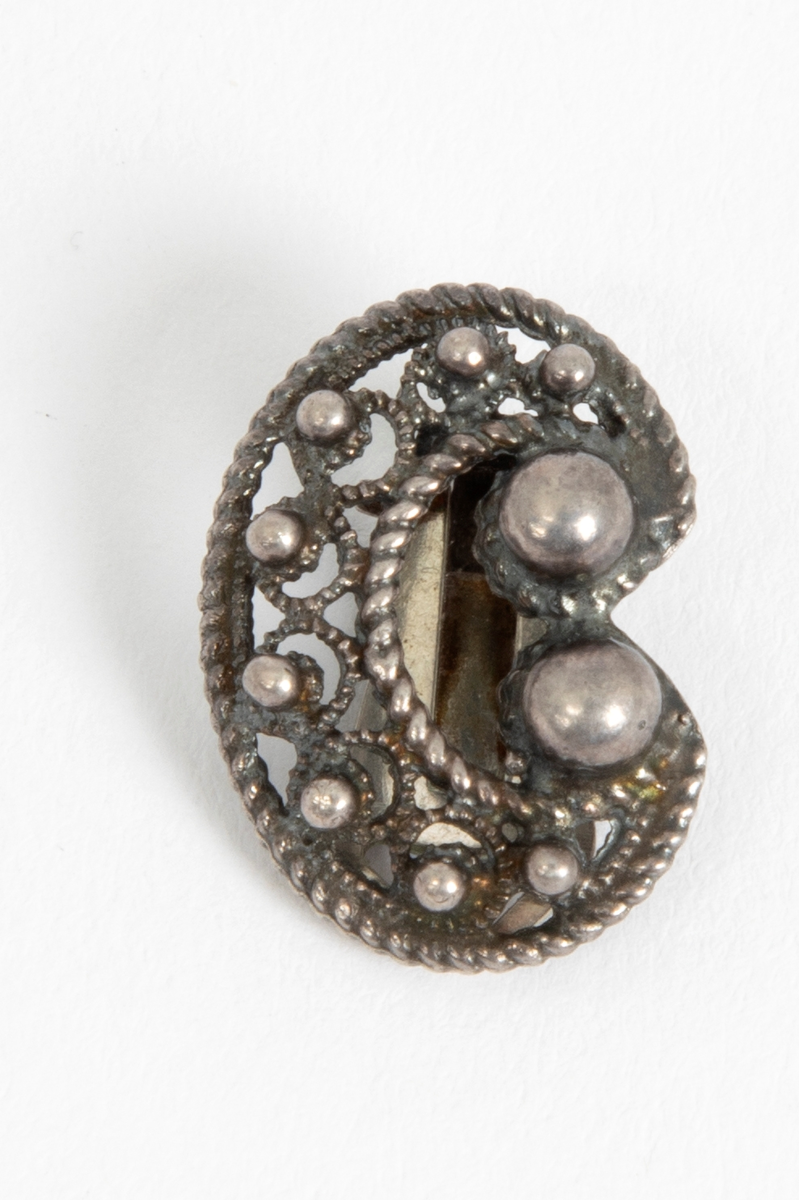En av to øreklips i sølv. C-formet med filigransarbeid, tvinnetråd langs kantene og åtte små og to større sølvperler.
