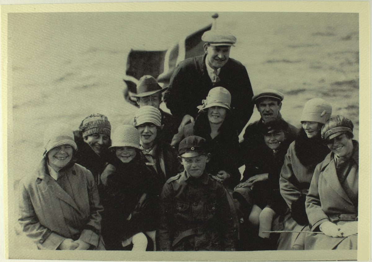 Gruppebilde av kvinner, menn og barn ombord i ein båt med flagg. Fleire av kvinnene har bøttehatt. Kvinna lengst til høgre har russehue og russestokk.