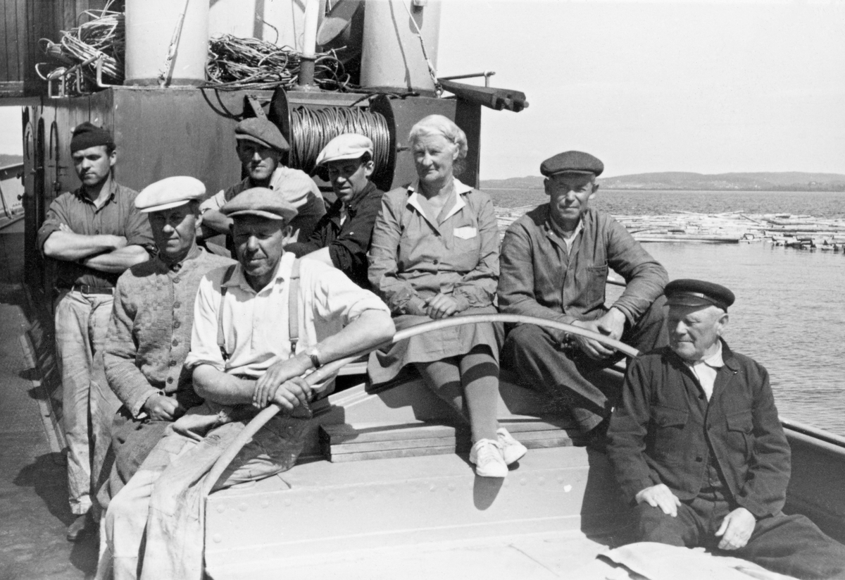 Mannskapet på slepebåten D/S Mørkfos i 1952.  Fotografiet viser sju menn og ei kvinne som fotografen har stilt opp på skylightet på båtdekket.  Samtlige er arbeidskledde.  Bak dem ses en trommel med vaier og nedre del av båtens skorstein.  Bakenfor båten skimtes en del buntet tømmer på vannspeilet. 

Slepebåten Mørkfos er 72 fot lang, og var den største båten i sitt slag på Øyeren.  Den ble bygd ved Glommen mek. verksted i Fredrikstad i 1912.  Oppdragsgiver var Fredrikstad tømmerdireksjon, som på denne tida organiserte tømmerfløtinga i Glommavassdraget sør for Fetsund.  Fra 1920 ble organisasjonen kalt Nedre Glommen fellesfløtningsforening.  Tidlig i 1940-åra ble tømmerfløtingsorganisasjonene i den øvre og den nedre delen av vassdraget slått sammen i Glomma fellesfløtingsforening.  Denne organisasjonen opptrådte som rederi for Mørkfos og en rekke andre slepebåter inntil fløtinga i vassdraget ble avviklet i 1985.  Mørkfos var opprinnelig dampdrevet, men i 1953 ble dampmaskinen tatt ut og erstattet av en tresylindret dieselmaskin, en Wickmann-motor.  Dermed ble båtens navn endret fra «D/S Mørkfos» til «M/B Mørkfos».   For ledelsen i Glomma fellesfløtingsforening var det antakelig viktigere at en etter denne ombygginga kunne redusere størrelsen på mannskapet noe.  Opprinnelig hadde det vært sju faste om bord: Skipper, to maskinister, tre dekksgutter og kokke.  Etter ombygginga til dieseldrift hadde Mørkfos et mannskap på fire-fem.  Den opprinnelige Wickmann-motoren fra 1953 ble for øvrig erstattet av en MWM-maskin (fra Motoren-Werke-Mannheim i den tyske delstaten Baden-Würtemberg) i 1966.  Mørkfos ble brukt til å slepe tømmer over Øyeren fra lensene på Fetsund i nord til Sandstangen i sør.  Der ble slepene med «sopper» (bunter) løst opp, og stokkene fikk gå fritt et stykke videre nedover i vassdraget, der det skulle passere flere kraftverk i trange tømmerrenner før det på nytt ble lenset, sortert og slept videre nedover vassdraget. 

Etter at fløtinga i Glommavassdraget ble avviklet ble M/B Mørkfos liggende ubrukt ved Fetsund lenser, der den forfalt.  I 1994 startet en venneforening et omfattende restaureringsarbeid, som ble støttet av Riksantikvarens avdeling for fartøyminnevern.  I 2004 ble restaureringsarbeidet belønnet med kulturvernprisen til Oslo/Akershus avdeling av Fortidsminneforeningen.  Båten drives av venneforeningen, som tilbyr sommerturer på Øyeren, med avganger fra lensemuseet på Fetsund.