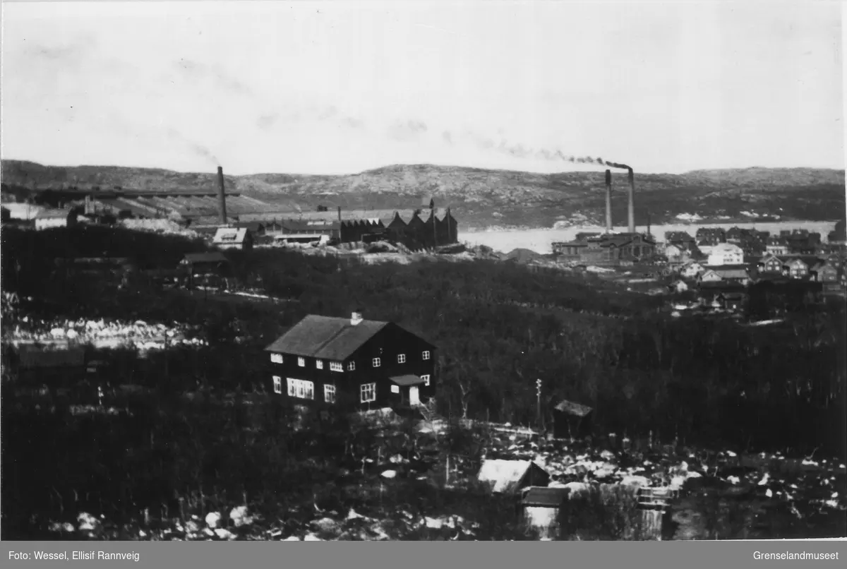 Bildet er tatt fra hvor der Pasvikveien ligger i dag med utsikt mot Doktorgården hvor ekteparet Andreas Wessel og Ellisif Wessel hadde tilhold.Til høyre ser man Kirkenes sentrum og på midten er industriområdet til A/S Sydvaranger. Bildet er tatt på 1920-tallet. 