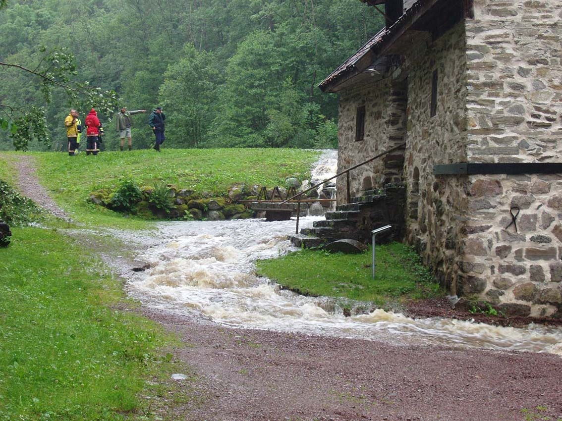 Vattnet rinner över dammen och forsar förbi Rasmus kvarn i Röttle. Personal från Räddningstjänsten står uppe vid dammen.