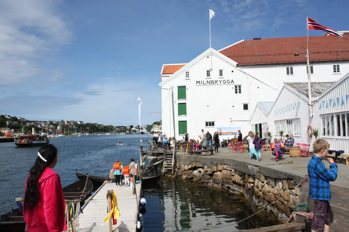 Bilde av front av norsk klippfiskmuseum sett fra brygga. Det er barn og voksne som myldrer rundt på et arrangement 